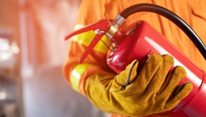 Technician in orange safety gear holding a red fire extinguisher during a fall fire safety inspection